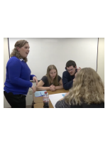 A female teacher standing with a group of students around a table in a classroom.