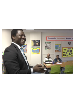 A male teacher standing before students sitting at a table in a classroom.